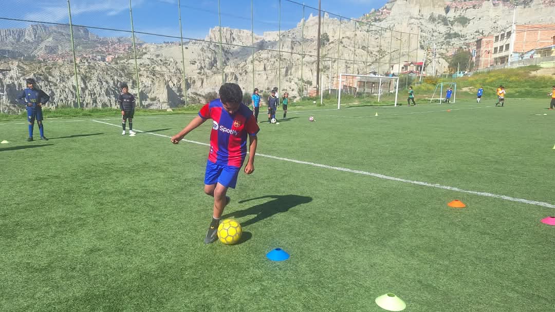 Una nueva esperanza para los futuros cracks del fútbol nació en Cotahuma. La Subalcaldía, junto con la Escuela de Deportes de la Alcaldía de La Paz, puso en marcha la Escuela de Fútbol Cotahuma (EFC), un proyecto completamente gratuito dirigido a niños y jóvenes de 8 a 18 años que sueñan con convertirse en profesionales del balompié. La iniciativa no solo busca mejorar el rendimiento deportivo de los participantes, sino también proyectarlos hacia clubes profesionales e incluso a la Selección Boliviana. “La idea es formar futbolistas desde temprana edad, brindarles condiciones adecuadas de entrenamiento y acompañarlos en su crecimiento”, explicó Javier Rodríguez, entrenador de la Escuela de Deportes La Paz. “El objetivo es claro: nutrir a las reservas de los grandes clubes”, añadió. Para muchos, como el pequeño Mario Cossío, esta escuela significa una puerta abierta hacia sus sueños. “Aprendí a jugar mejor, quiero ir al exterior, jugar partidos internacionales y llegar a un Mundial como Ronaldinho”, expresó con emoción. Desde la Subalcaldía, también se destaca el componente social del proyecto. Rubén Callisaya, técnico de la Unidad de Desarrollo Económico y Social, resaltó la importancia de descubrir talentos que puedan competir a nivel nacional e internacional. “Queremos innovar, motivar e impulsar a que más jóvenes encuentren en el deporte una opción de vida”, señaló. Los padres también celebran la iniciativa. Tatiana Sánchez, madre de uno de los inscritos, agradeció el impulso a la disciplina deportiva en la zona. “Esta escuela aleja a los chicos de los vicios, les da una rutina saludable y los mantiene enfocados en algo positivo”, dijo. Hasta el momento, la Escuela de Fútbol Cotahuma ya cuenta con 25 niños y 40 jóvenes inscritos. La puerta está abierta para todos los que deseen mejorar, entrenar y soñar en grande. Porque en Cotahuma, el futuro del fútbol se está formando desde la base.